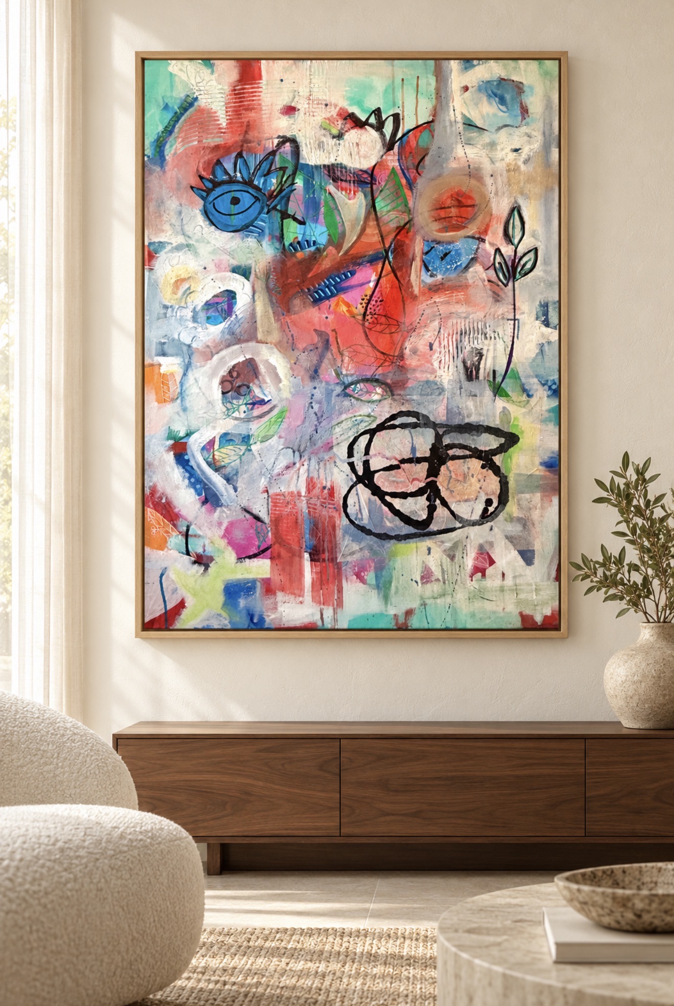 A Curious Kind of Knowing, a colorful mixed-media painting with eye and botanical motifs, framed above a wooden cabinet in a sunlit room